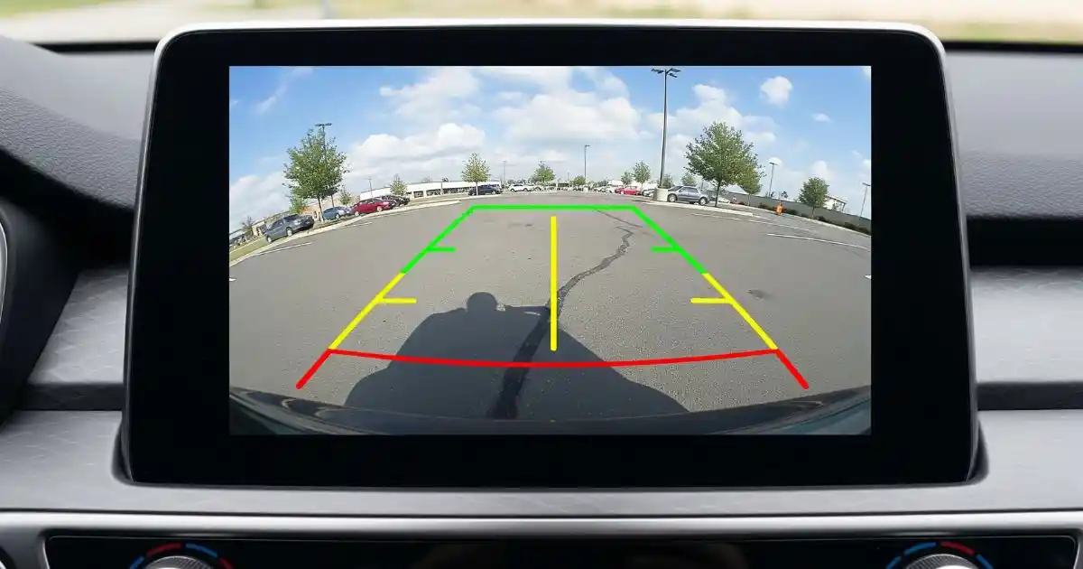 The view from a backup camera on a car's screen, showing a parking lot with safety lines.